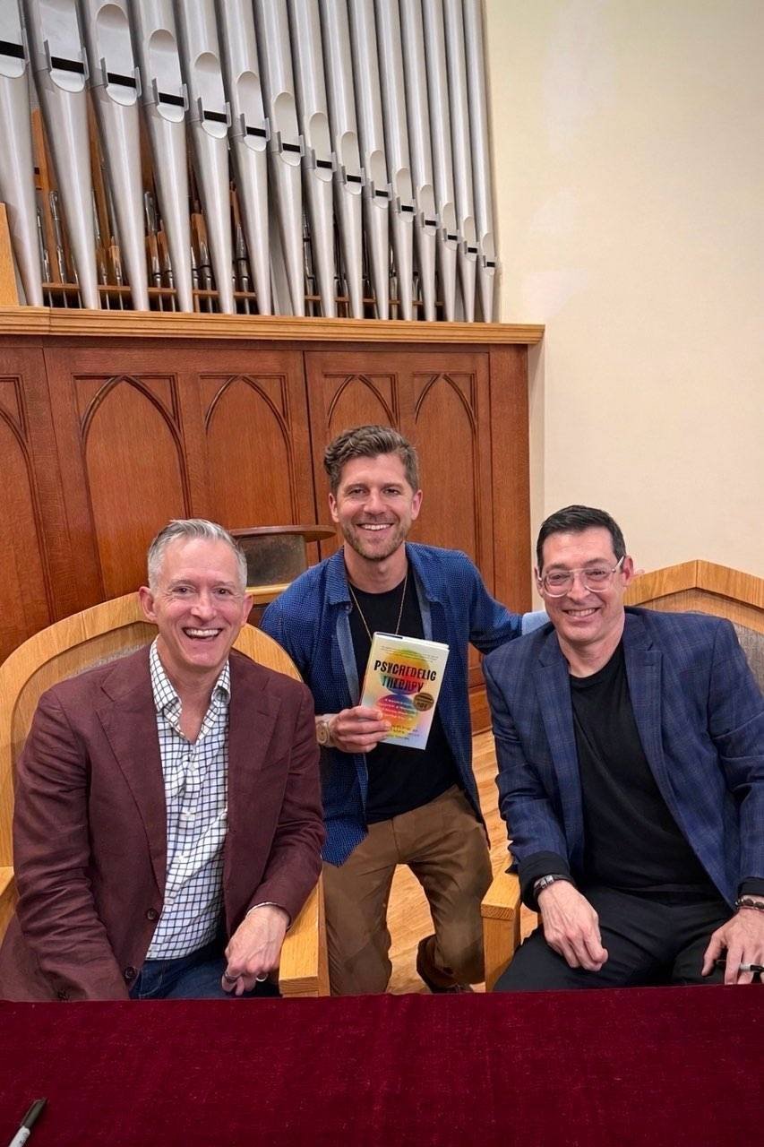 Julian holding the Psychedelic Therapy book with two guests at a church event